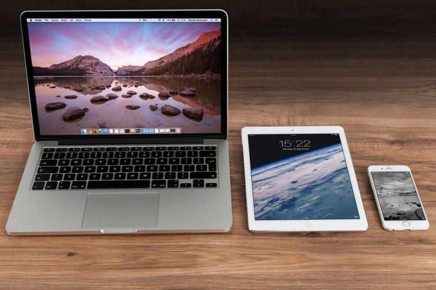 3 appareils Apple : ordinateur portable, tablette et smartphone sont alignés sur une surface en bois